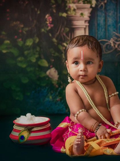 A baby boy portrayed as the infant Krishna, complete with pearl necklaces and a pot of white butter, showcasing a classic and adorable theme.