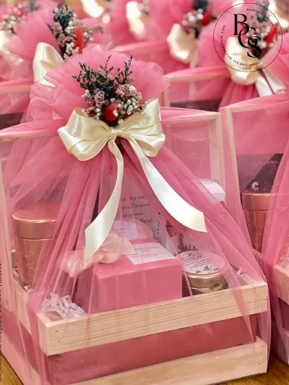 A closer look at our popular pink-themed hamper. A rustic wooden crate filled with goodies is enveloped in soft pink tulle, tied with a cream ribbon, and adorned with a small bouquet of dried flowers.