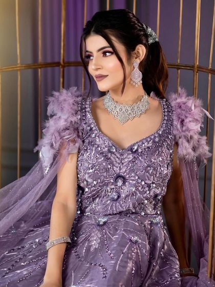 A stunning model in a lavender cocktail gown with feather details. The makeup is magical, with purple glittery eyes and a matching lip color.