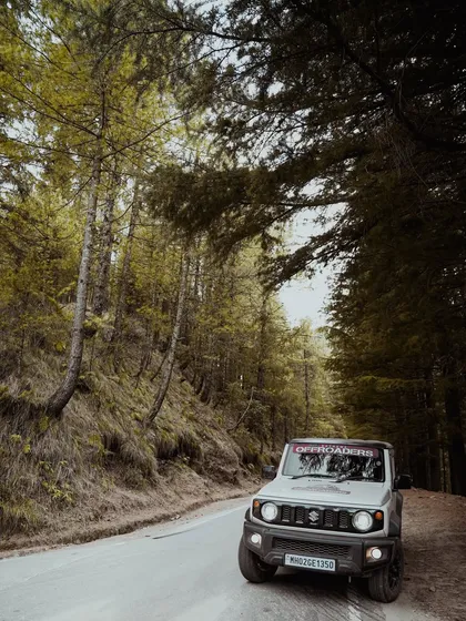 Parked on a quiet stretch of road surrounded by tall pine trees, this white Suzuki Jimny looks right at home in the wilderness. This shot highlights the vehicle's connection to nature and exploration.