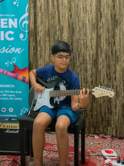 A young student plays his electric guitar with a Marshall amplifier visible, showing a complete rock setup.