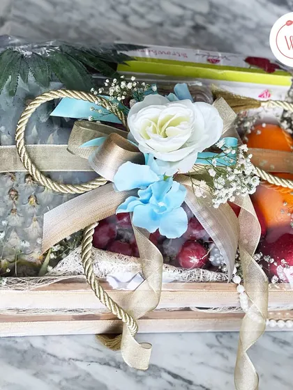 A rustic wooden crate filled with fresh fruits like pineapple and grapes, wrapped beautifully with a large bow.