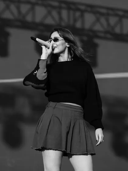 A black and white shot from a sound check. Dhvani Bhanushali in a casual pleated skirt and sweater, capturing the focused yet relaxed energy of pre-show preparations.