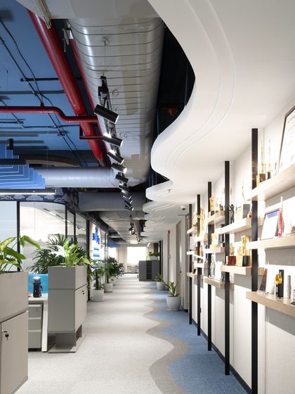 A key feature of the office is this corridor, where a custom shelving unit proudly displays the company's awards. The flowing wave pattern on the floor guides movement through the space, connecting different zones seamlessly.