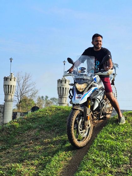 A rider and his bike on a grassy hill, with the unique castle-like structures of The KGF Trails in the background. Our training locations offer both great challenges and scenic views.