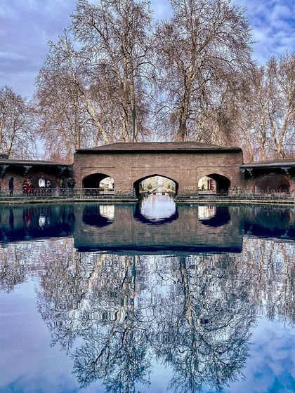 A perfect reflection of the Mughal arcade and bare trees in the crystal-clear water of Verinag spring. The stillness of the water creates a mirror to another world.