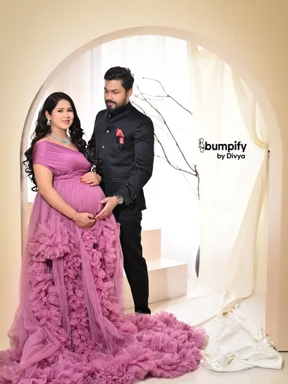 The dad-to-be joins his partner for a classic couple's portrait. His dark suit provides a beautiful contrast to her voluminous pink gown in this elegant studio shot.