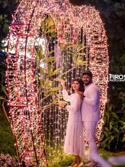 A fun and casual shot of a couple in all-white outfits in front of the large, illuminated heart prop.
