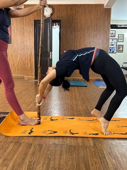 Using a staff as a prop can provide the stability needed for a deep wheel pose drop-back. This technique helps build strength and trust in your body's abilities.