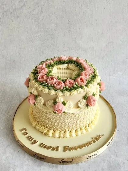 A beautiful two-tiered cake with classic English buttercream piping. The delicate pink roses and green wreath design give it a vintage, elegant feel.