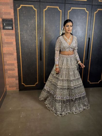 A full-length shot of a model in a silver-grey lehenga in a modern interior setting.
