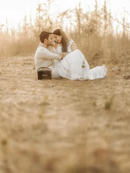An intimate moment in a sun-drenched field. The couple sits close together, sharing a quiet connection, with their music speaker nearby setting the mood for their outdoor shoot.