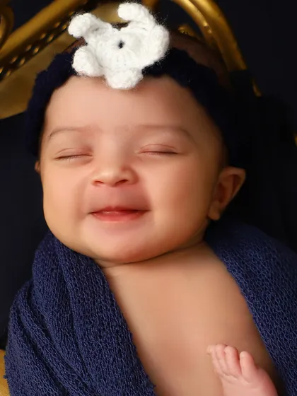 A beautiful, sleepy smile from a newborn wrapped in a deep blue cloth. Capturing these fleeting dream-smiles is what makes newborn photography so special.