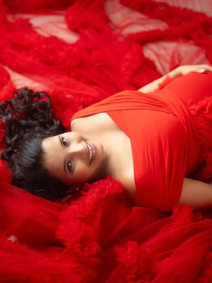 A portrait of pure radiance. Lying on a bed of vibrant red fabric, this mom-to-be’s joyful smile and glowing skin are the centerpiece of this beautiful studio shot.