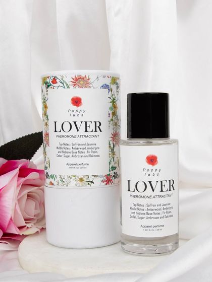 A creative shot of 'Lover' perfume with its floral-designed packaging, styled with a pink rose and white satin to evoke a romantic and luxurious feeling.