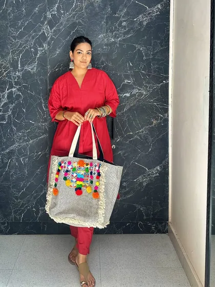Here is a full view of the pom-pom tote paired with a bright red kurta. The colorful tassels and mirror work add a playful, bohemian touch to the traditional outfit.