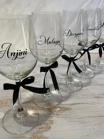 A set of elegant personalised wine glasses, perfect for raising a toast with your bridesmaids. Each glass is customised with a name in a beautiful script font and tied with a simple black ribbon.