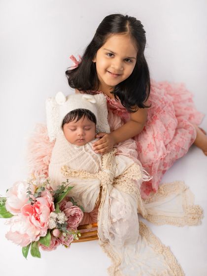 A beautiful newborn and sibling portrait with a soft, romantic theme. The pink tones and floral elements create a delicate and sweet image.