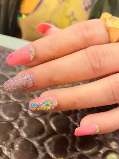 A close-up of a detailed nail art design. This image highlights a pink nail with a textured, multi-colored crystal embellishment, showing the intricate placement of each stone.