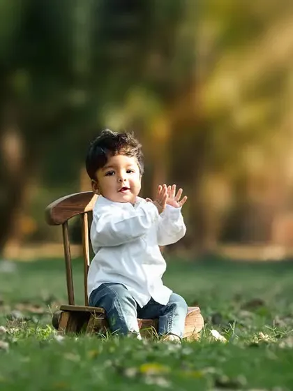 A portrait of a toddler sitting on a small wooden chair in a park. The beautiful backlighting from the sun creates a warm, golden glow.
