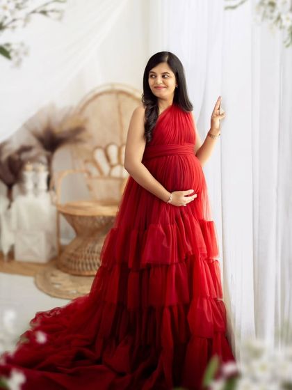 A serene portrait by the window, using natural light to highlight the vibrant red of the gown and the mother's glow.