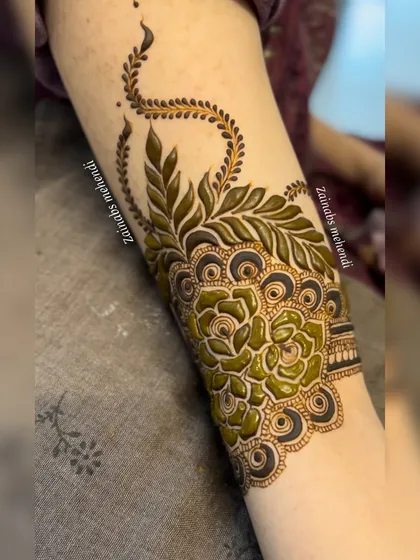 A close-up of the fresh henna paste on Ameena's arm, showcasing a beautiful Pakistani design with bold leaves and roses.