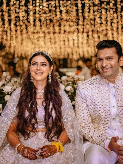 The bride and groom seated amidst a sea of white flowers and fairy lights, enjoying the Sangeet performances.