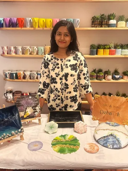 A student displays a variety of her finished resin art pieces, including coasters, trays, and a personalized nameplate, showing the versatility of the medium.