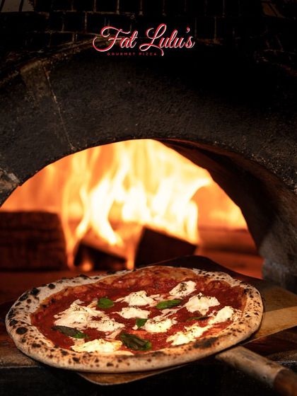 A classic Margherita pizza with fresh mozzarella and basil is about to be cooked by the flames of the wood-fired oven. The high heat is key to that authentic Neapolitan style crust.