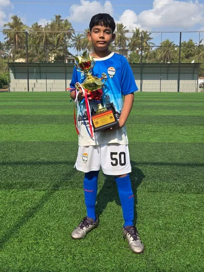 An U12 player proudly displays his trophy against the backdrop of the Goa football ground.
