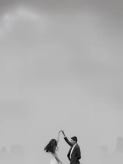 A minimalist black and white shot of a couple dancing against a hazy city skyline. The vast negative space emphasizes their solitary dance, creating a feeling of romance and timelessness.