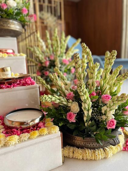 A close-up of a traditional brass planter filled with fresh tuberoses and roses, placed on a bed of jasmine and marigold petals. This type of arrangement is perfect for adding fragrance and beauty to home festivities.