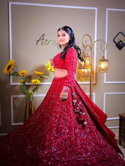 A full-length shot of a bride in a sparkling red lehenga, taken in a studio setting with warm, ambient lighting.