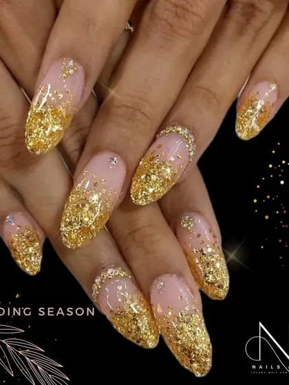 Nothing says celebration like gold glitter. This stunning wedding season look features long, almond-shaped nails with a nude base and a heavy cascade of chunky gold glitter from the tips.