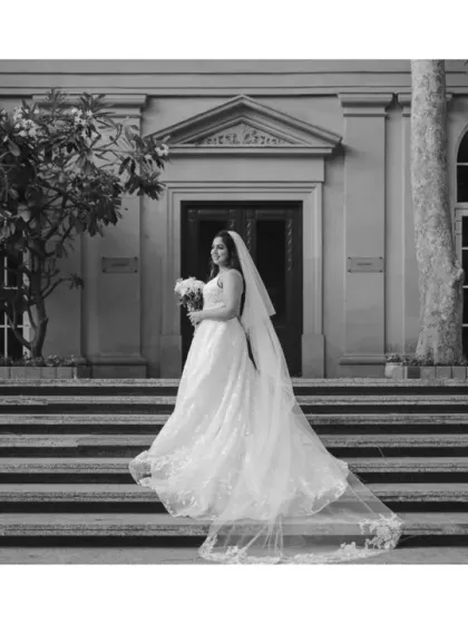 A timeless black and white portrait of the bride on the steps of the historic building. Her elegant white gown and long veil create a classic, graceful silhouette.