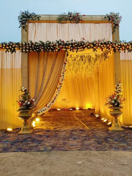 A complete view of the lit wedding entrance at dusk, ready to welcome guests. The setup includes the main structure, pathway lighting, and floral urns.