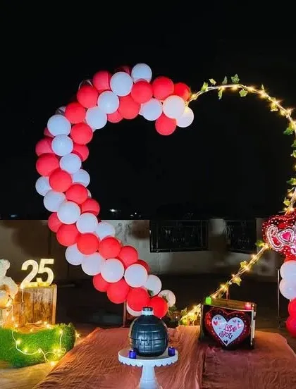 A beautiful terrace setup for a 25th anniversary or birthday. The heart-shaped balloon arch is lit with fairy lights, and the scene is completed with a teddy bear and light-up numbers.