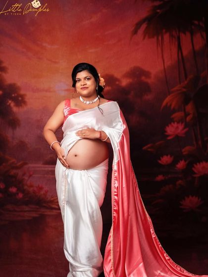 The glow of motherhood is so precious. This mom-to-be looks radiant in her white and pink satin saree against a painterly backdrop.