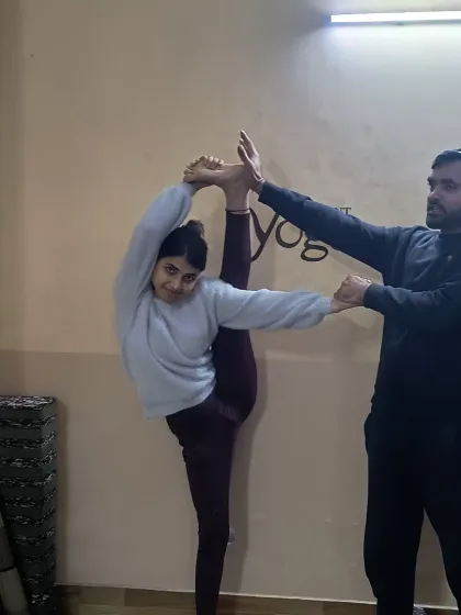 An instructor provides support as a student works towards the full expression of Trivikramasana (Standing Splits). This advanced pose requires immense hamstring flexibility and balance, and we guide our students through every step of the process.