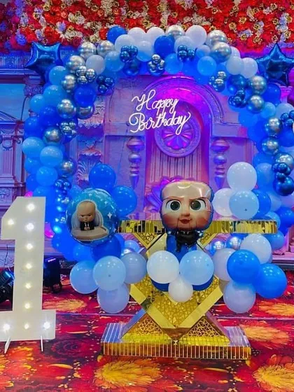 A fun and detailed 'Boss Baby' themed first birthday party. This setup includes custom character cutouts, a large light-up number 'one', and a coordinated blue and silver balloon arch.