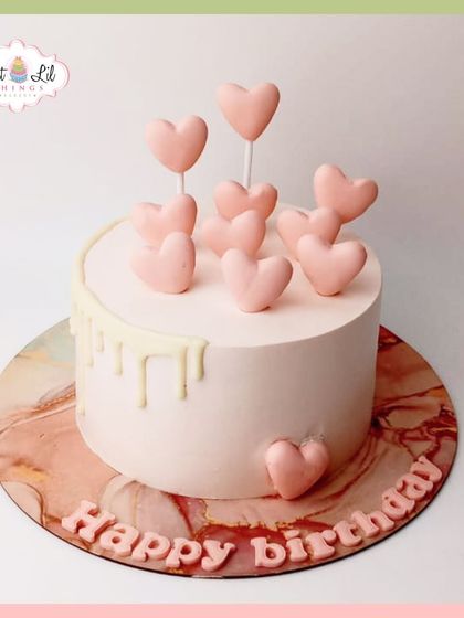 A simple and sweet birthday cake covered in pink hearts and a white chocolate drip.