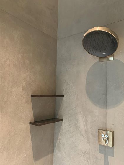 A detail from a modern shower, featuring micro-cement walls and a brushed gold fixture. The combination of raw texture and refined metal creates a sophisticated, sensory experience.