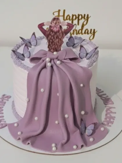 An elegant cake featuring a flowing lilac gown made of fondant. This preservative-free, 100% eggless cake is decorated with butterflies and pearls for a sophisticated birthday celebration.
