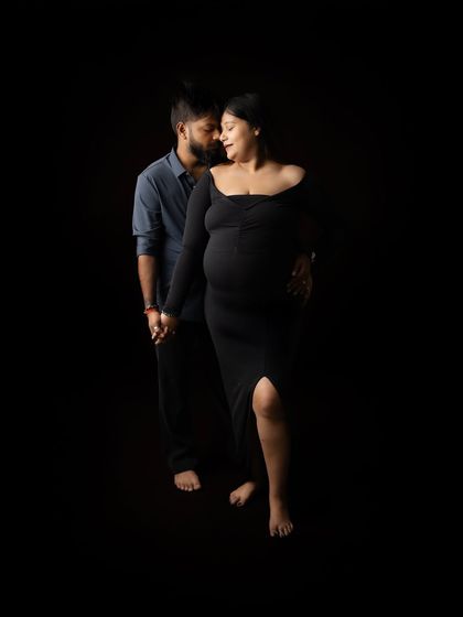 A full-length shot of the couple holding hands. The dark, minimalist setting puts all the focus on their connection and the silhouette of the baby bump.