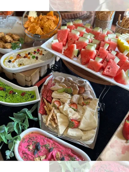 A vibrant display of our colorful dips, including beetroot hummus and edamame hummus, served alongside fresh pita, watermelon slices, and nachos. It's a healthy, beautiful, and delicious part of any grazing table.