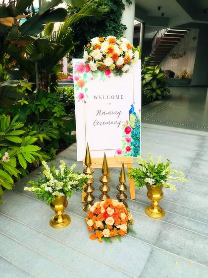 A custom welcome board for a naming ceremony, decorated with fresh flowers. The design features a peacock motif, adding a touch of traditional artistry to the entrance.