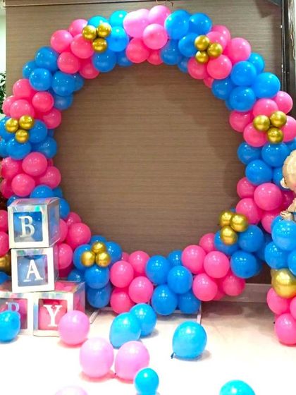 A bright and cheerful baby shower balloon ring in pink and blue. The setup includes 'BABY' blocks and cute baby-shaped foil balloons on either side.