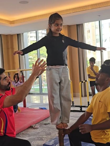 A child bravely balances on the Mallakhamb pole with the help of two coaches. This traditional Indian sport is an amazing test of balance, strength, and focus.