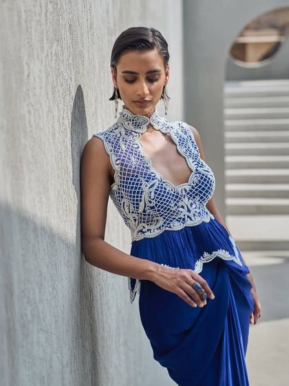 Sculpted in Active Blue, this pearl-kissed silhouette moves like poetry. The design features a high-neck, pearl-embellished bodice with a peplum detail, paired with a draped skirt.