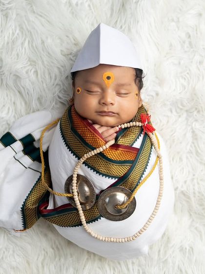 Dressed as a little Warkari devotee, this baby is styled with a Gandhi cap, a shawl, and tiny cymbals on a soft white fur backdrop. It's a serene and soulful concept.